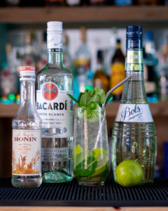 The cucumber mojito cocktail on a home bar top, surrounded by its ingredients.