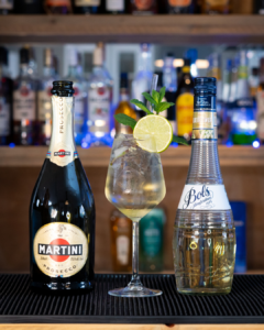 The Hugo Spritz cocktail on a home bar top, surrounded by its ingredients