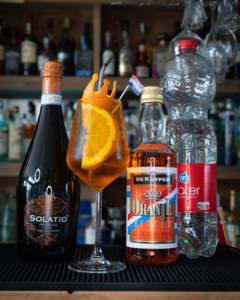 The Kingsday Spritz cocktail on a home bar top surrounded by its ingredients
