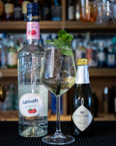 The Lychee Spritz Cocktail on a home bar top surrounded by its ingredients