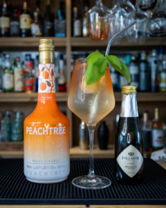 The Peach Spritz cocktail on a home bar top, surrounded by its ingredients