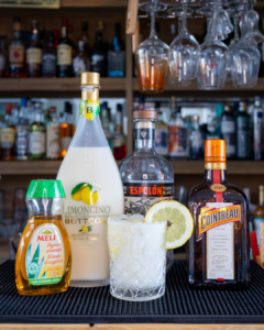 The Creamy Limoncello Margarita cocktail on a homebar top, surrounded by its ingredients.