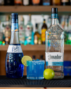 The Margarita Azul cocktail on a homebar top, surrounded by its ingredients.