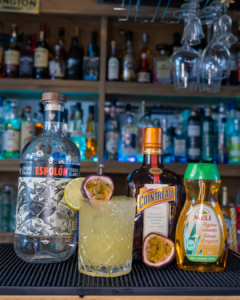 The Passionfruit Margarita cocktail on a home bar top surrounded by its ingredients