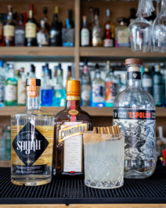 The Spekkoek Margarita cocktail on a homebar top, surrounded by its ingredients.