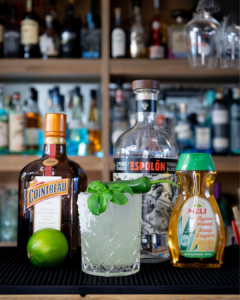 The Spicy Basil Margarita cocktail on a homebar top, surrounded by its ingredients.