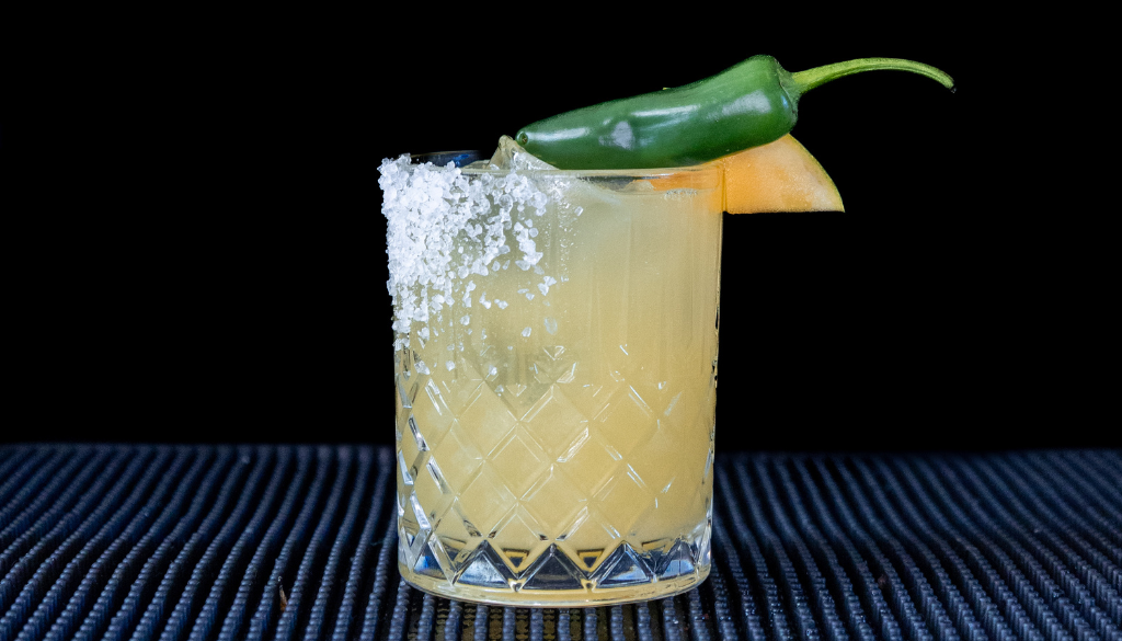 The Spicy Mango Margarita cocktail on a homebar top, with an all black background