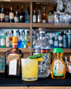 The Spicy Mango Margarita cocktail on a homebar top, surrounded by its ingredients.