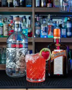The Margarita Azul cocktail on a homebar top, surrounded by its ingredients.