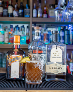The Tropical Coffee Margarita cocktail on a homebar top, surrounded by its ingredients.