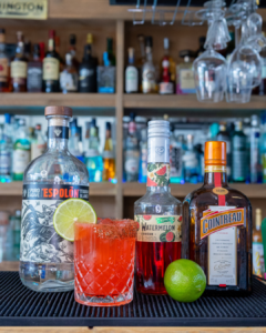 The Watermelon Margarita cocktail on a homebar top, surrounded by its ingredients.