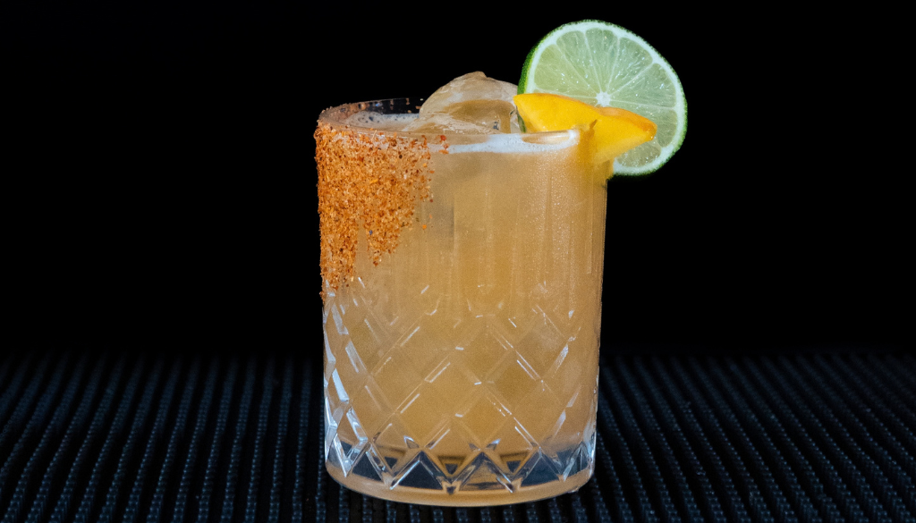 Hot Honey Peach Margarita cocktail on a home bar top with an all black background