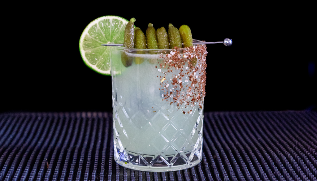 The Pickle Margarita cocktail on a home bar top with an all black background