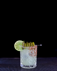 The Pickle Margarita cocktail on a home bar top with an all black background