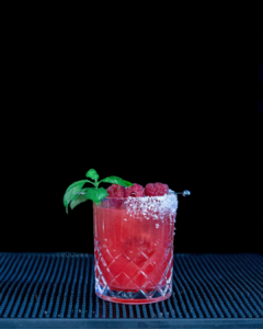 The Raspberry Basil Margarita cocktail on a home bar top with an all black background