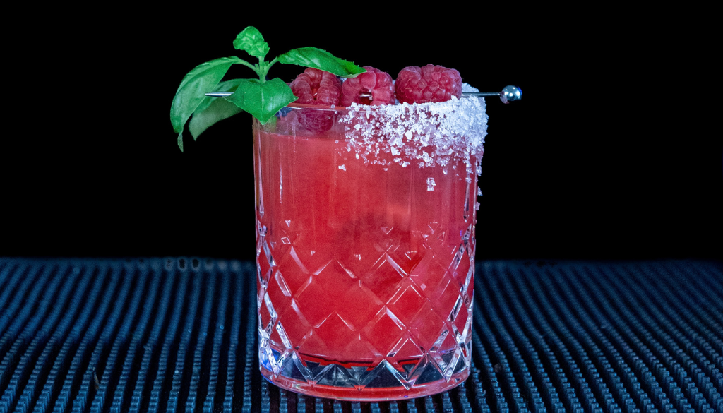 The Raspberry Basil Margarita cocktail on a home bar top with an all black background