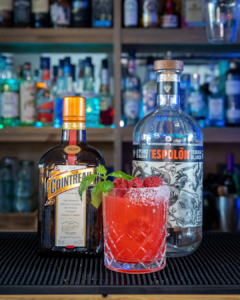 The Raspberry Basil Margarita cocktail on a home bar top surrounded by its ingredients